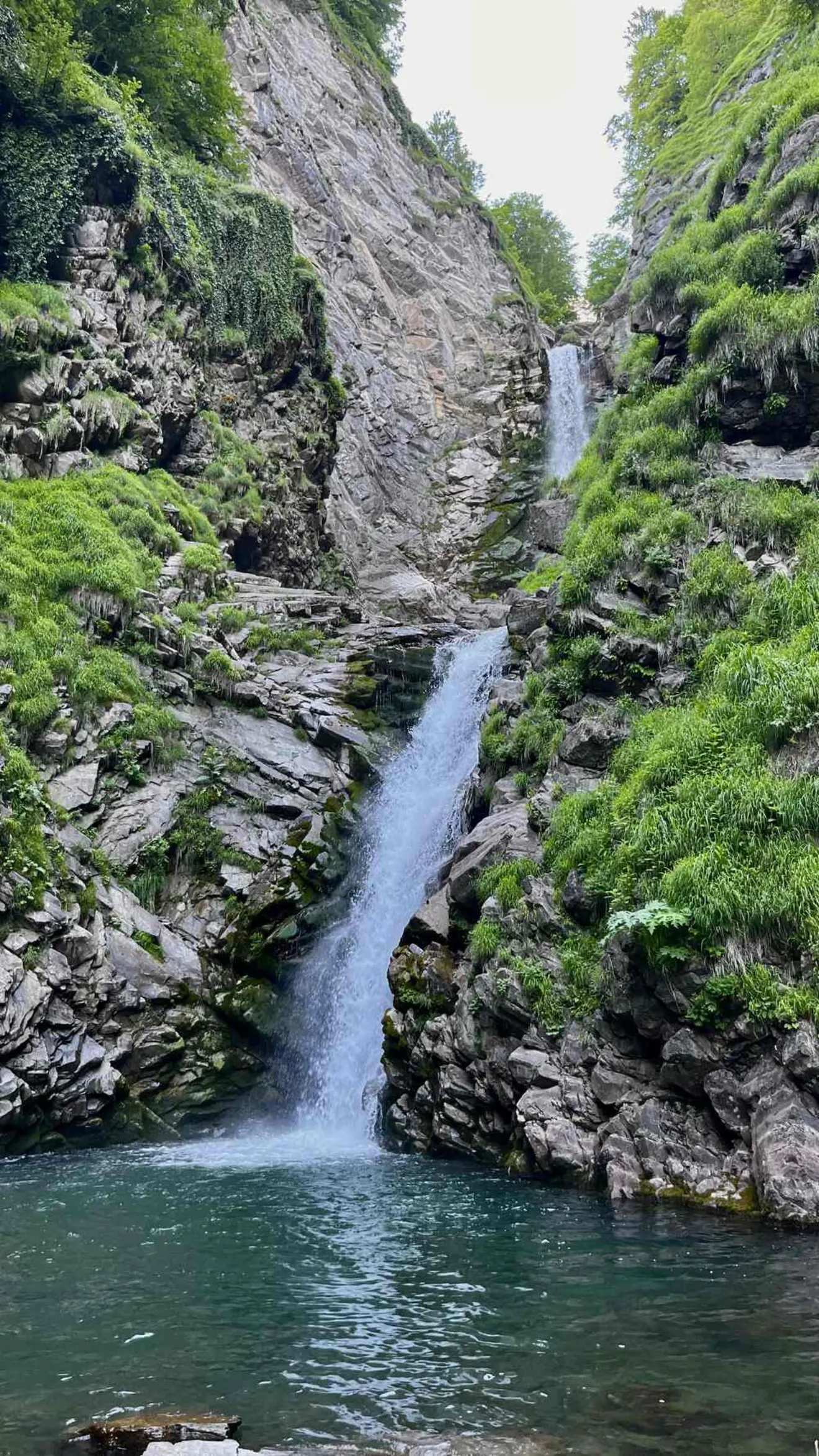 Двухступенчатый водопад падает в горное ущелье среди зелени