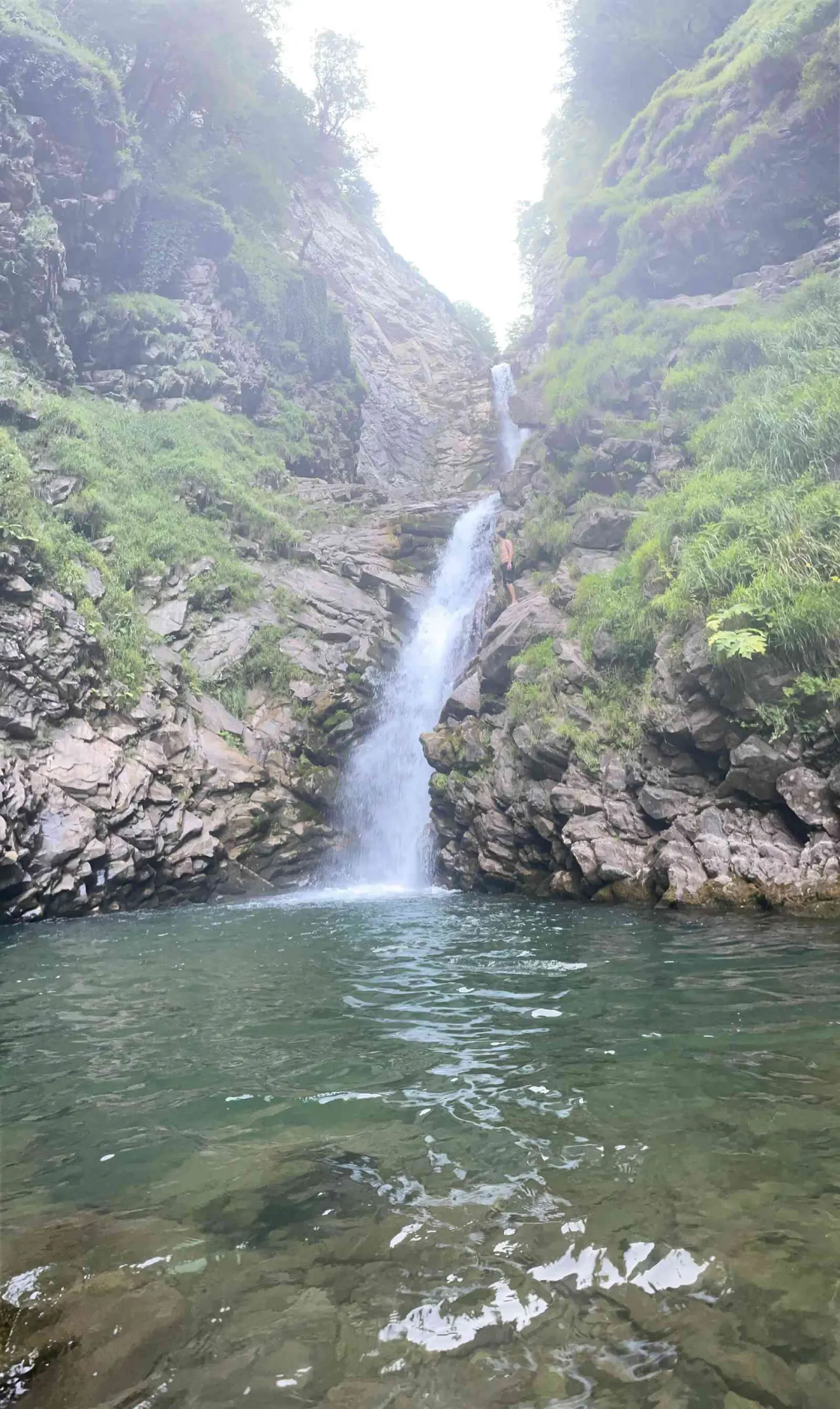 Водопад падает в горное ущелье, человек стоит рядом на скале