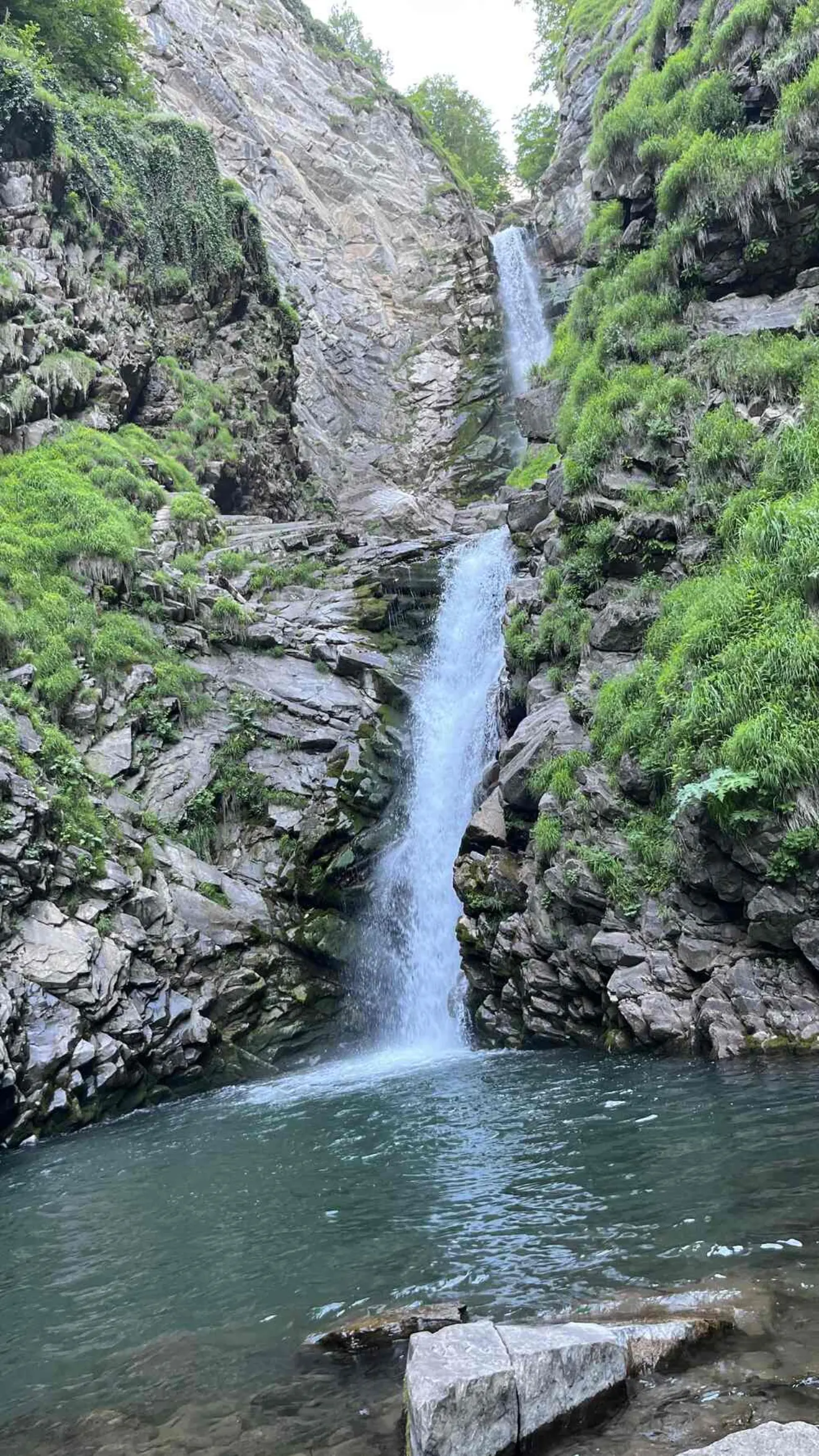 Два каскада узкого водопада стекают по скальному ущелью среди зелени